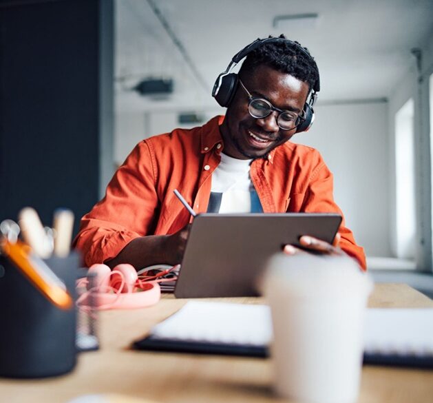A smiling learner with headphones writing on a tablet